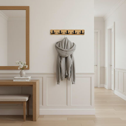 Minimalistyczny przedpokój z zamontowanym na ścianie dębowym wieszakiem o długości 50 cm z czarnymi haczykami.