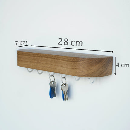 Zdjęcie dębowej półki na klucze z nałożonymi infografikami wymiarów: długość 28 cm, głębokość 7 cm i grubość 4 cm, ilustrując jej optymalne, kompaktowe proporcje.