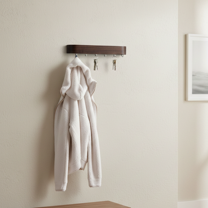 Elegancki, minimalistyczny wieszak wykonany z  drewna orzecha amerykańskiego o wyraźnym usłojeniu i zaokrąglonych krawędziach. Pod spodem znajduje się sześć metalowych haczyków, na których wiszą pęki kluczy oraz biała, puszysta bluza.