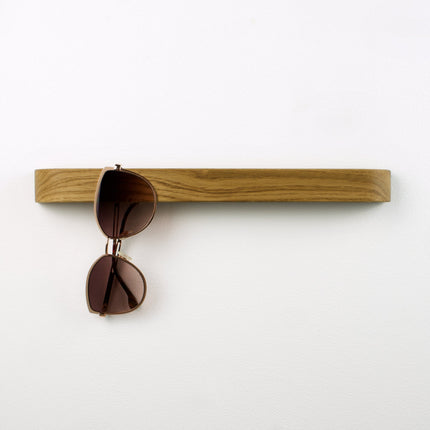 Drewniany wieszak na okulary z litego dębu zamontowany na ścianie, minimalistyczny design i naturalna faktura drewna.